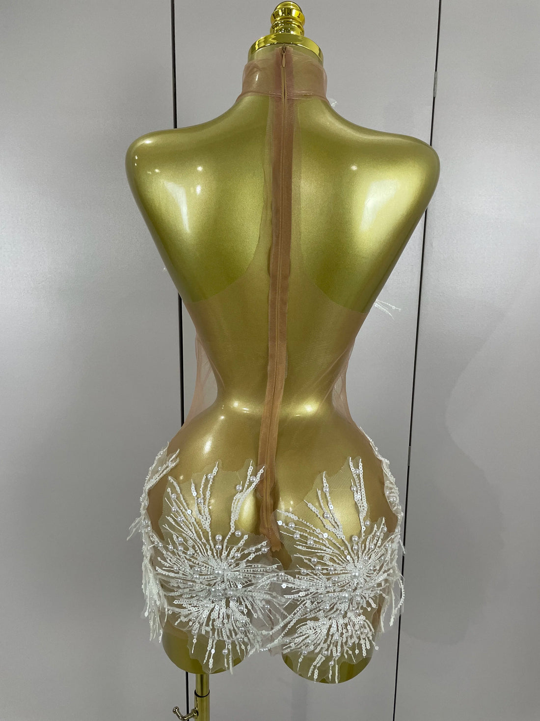 Gold mannequin wearing a sheer white bikini with floral details against a plain background